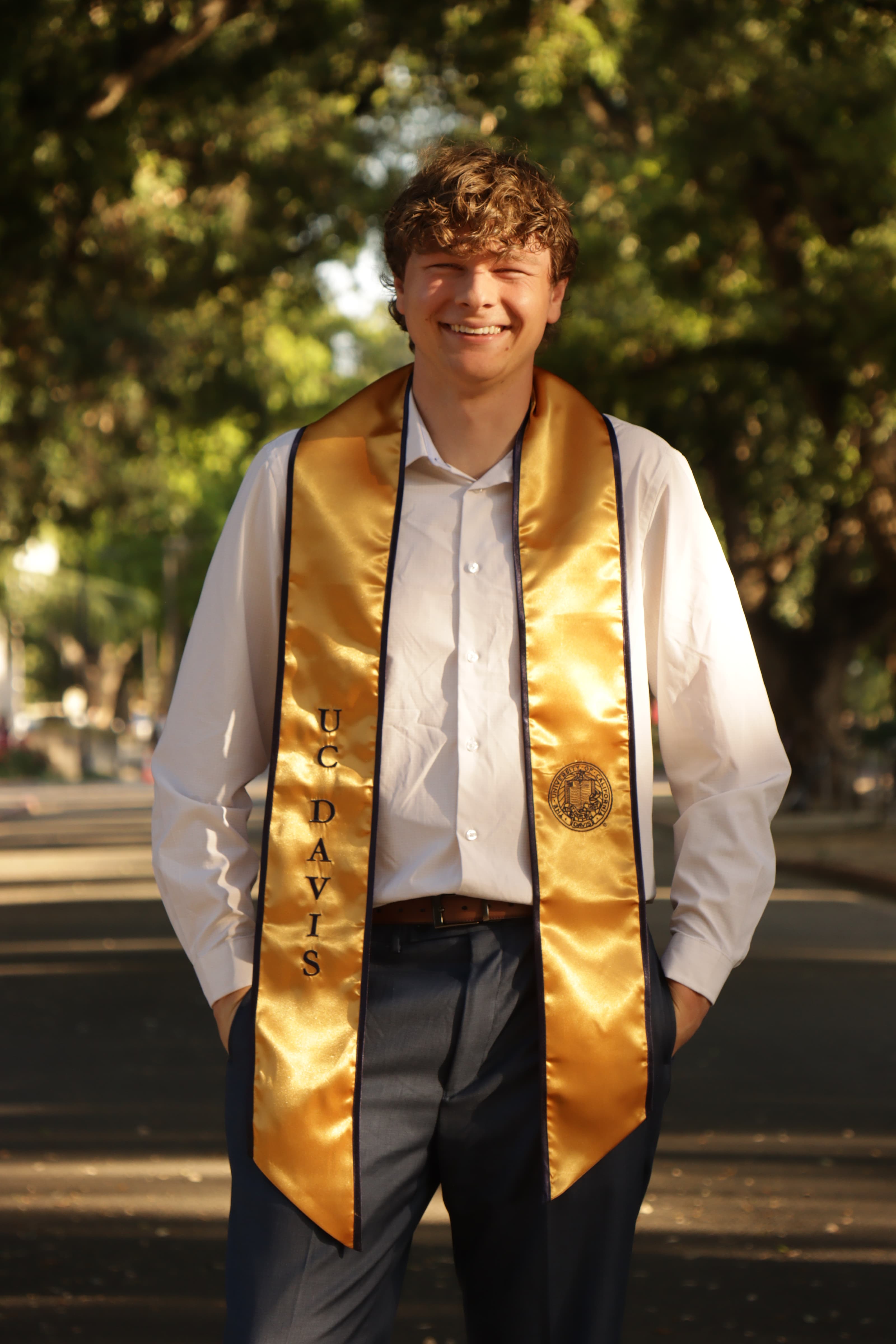Aidan smiling outdoors in a gold graduation stole