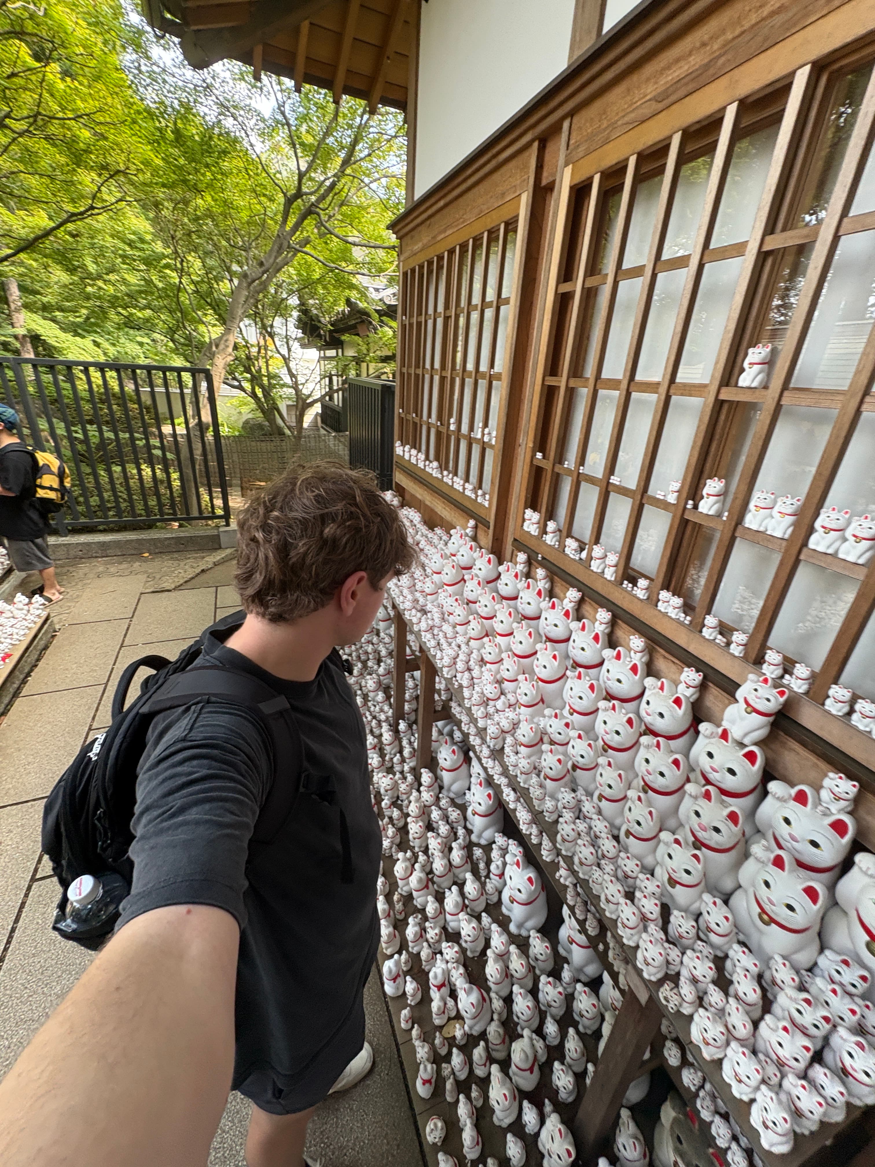 Aidan visiting a wall of maneki-neko figures in Japan